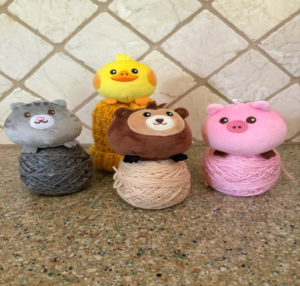 A selection of the available Farmyard Hat yarn kits. Shown animals are a grey cat, brown bear, yellow duck, and pink pig.