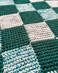 An image showing a series of joined squares made with Tunisian crochet. The squares are a variety of green, tan, and a variegated blue color.
